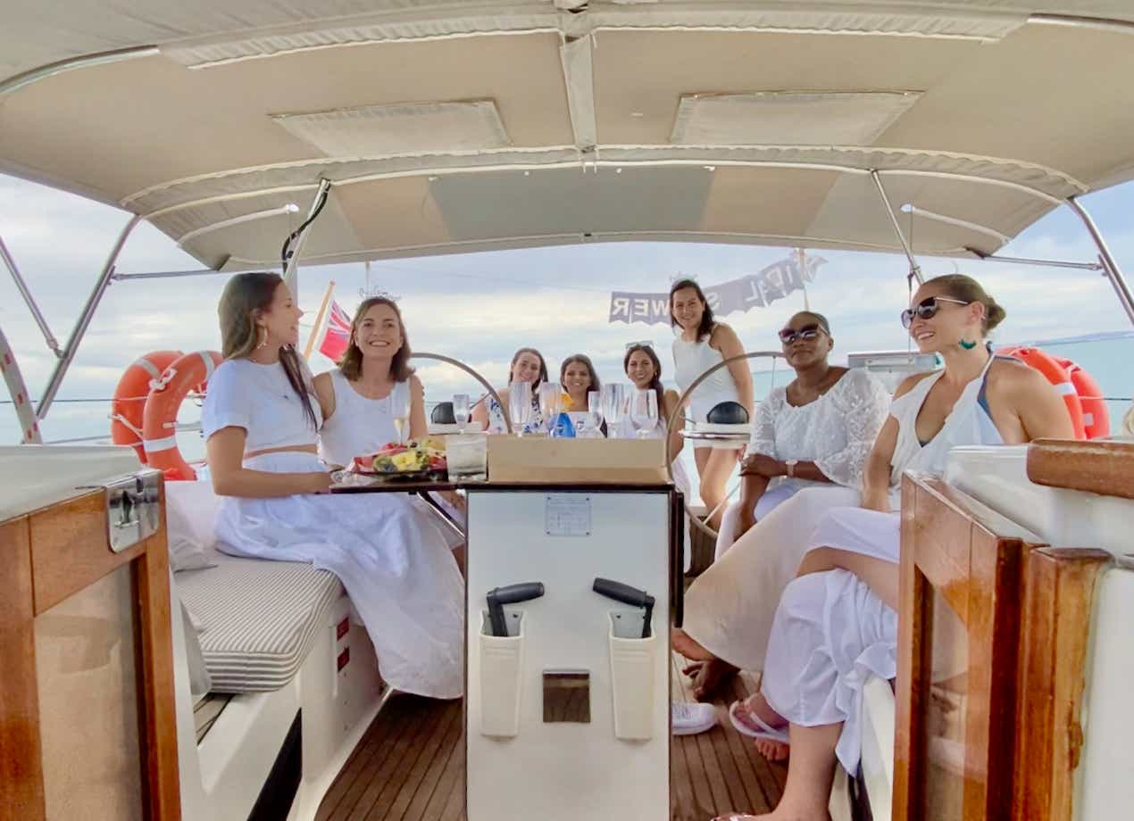 Hens party with hens all dressed in white sitting on the private yacht.